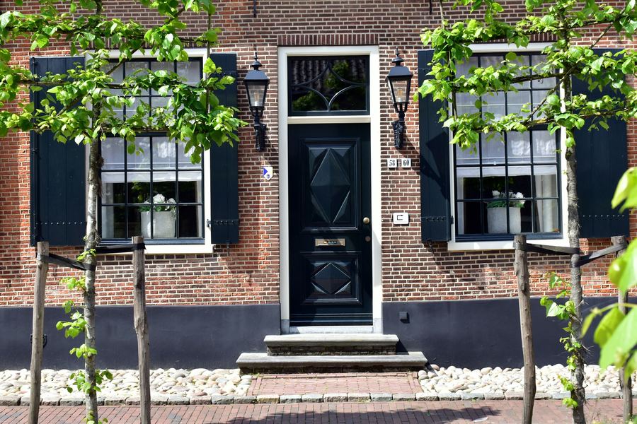 Black front door of a Dutch brick house with shutters and young trees